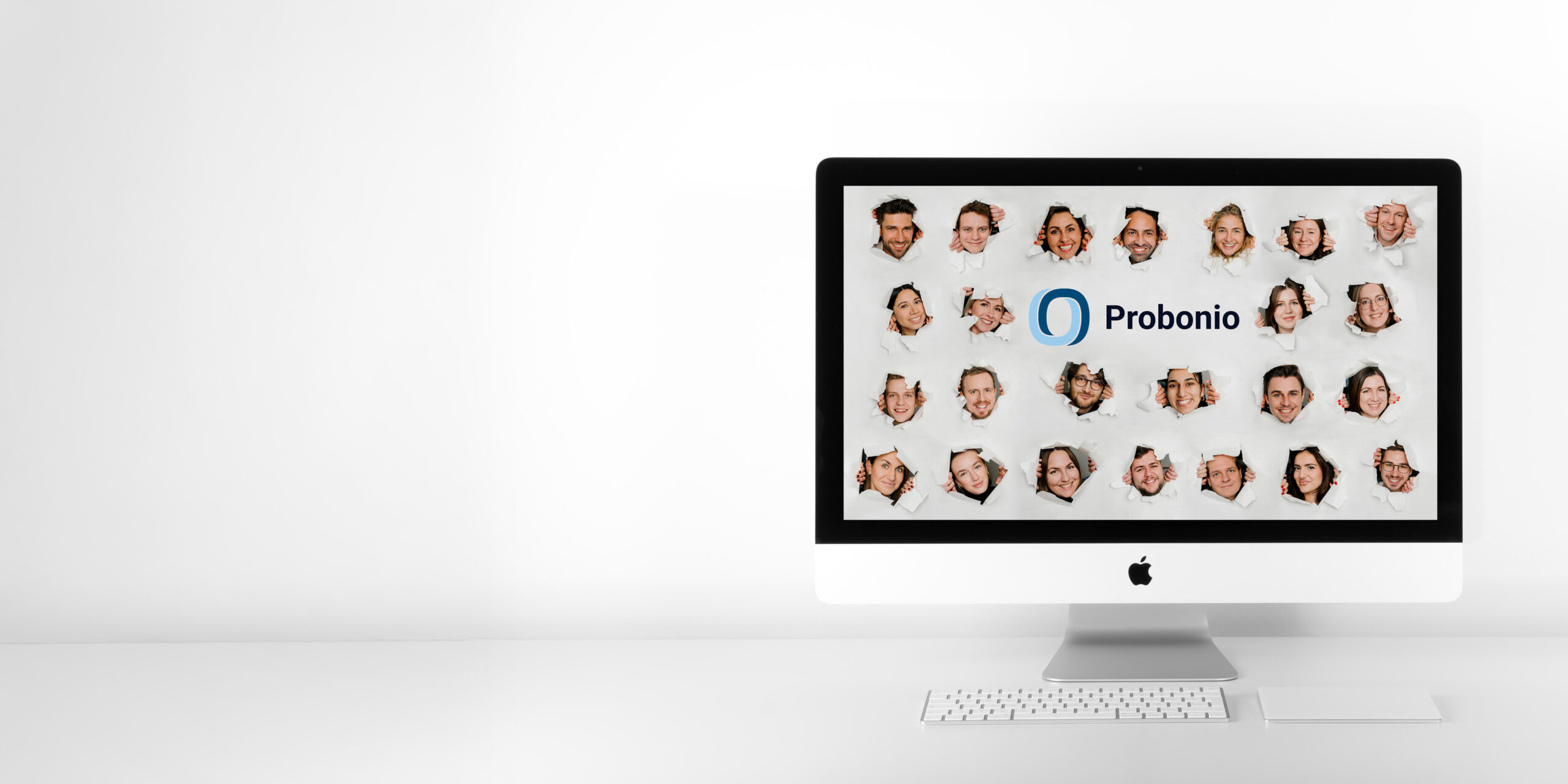 Ein iMac steht auf einem weißen Schreibtisch vor einer schlichten Wand. Auf dem Bildschirm sind das Logo und der Name von Probonio zu sehen, umgeben von verschiedenen Kopfbildern lächelnder Menschen auf weißem Hintergrund.