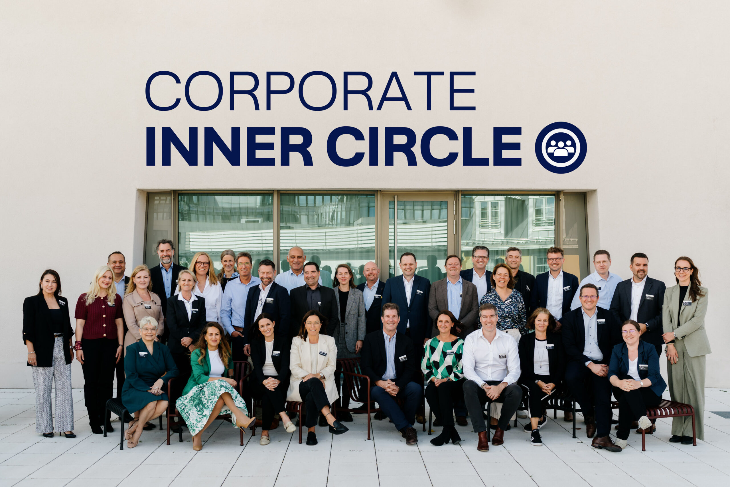 Eine Gruppe von etwa 40 professionell gekleideten Personen posiert draußen vor einer beigen Wand mit der großen Aufschrift CORPORATE INNER CIRCLE und einem kreisförmigen Symbol mit drei Personen.