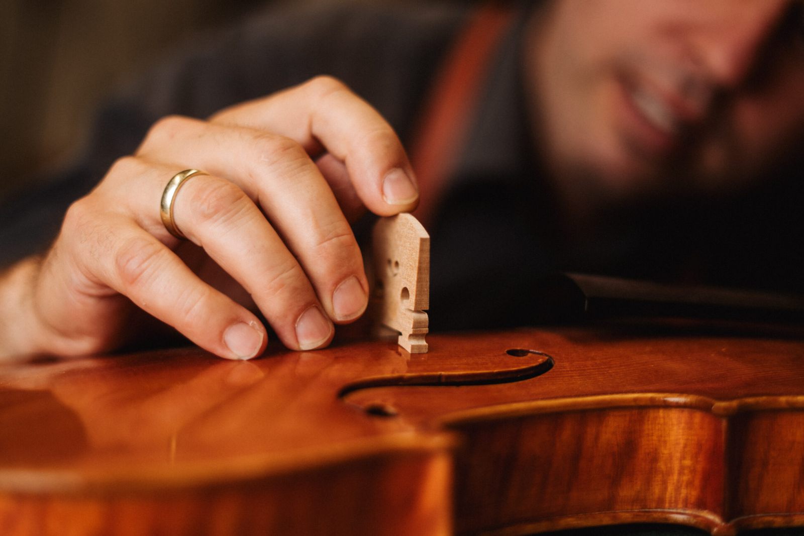 Eine Person setzt den Steg vorsichtig auf eine Geige und konzentriert sich dabei auf die feinen Holzdetails des Instruments. Nur die Hand der Person und ein Teil ihres Gesichts sind sichtbar.