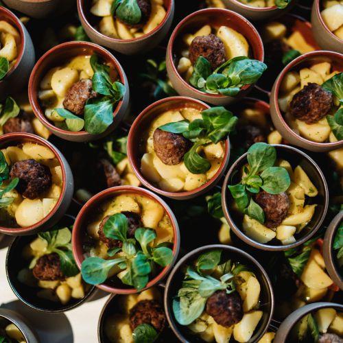 Mehrere kleine Tassen sind mit Nudeln, Fleischbällchen, frischem Gemüse und Gemüsewürfeln gefüllt, die dicht beieinander liegen und ein farbenfrohes und appetitliches Bild ergeben.