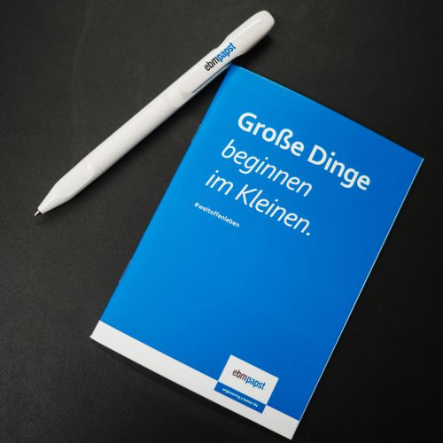Ein weißer Stift und ein blaues Notizbuch auf einer schwarzen Fläche. Auf dem Umschlag des Notizbuchs steht "Große Dinge beginnen im Kleinen", unten ist das Logo "Stiftungsrat" zu sehen.