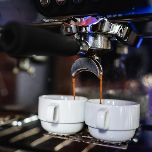 Nahaufnahme einer Espressomaschine, die Kaffee in zwei weiße Keramiktassen gießt, die nebeneinander unter den Ausläufen stehen. Die Maschine und die Tassen sind scharf abgebildet und heben die reichhaltigen Espressoströme hervor.